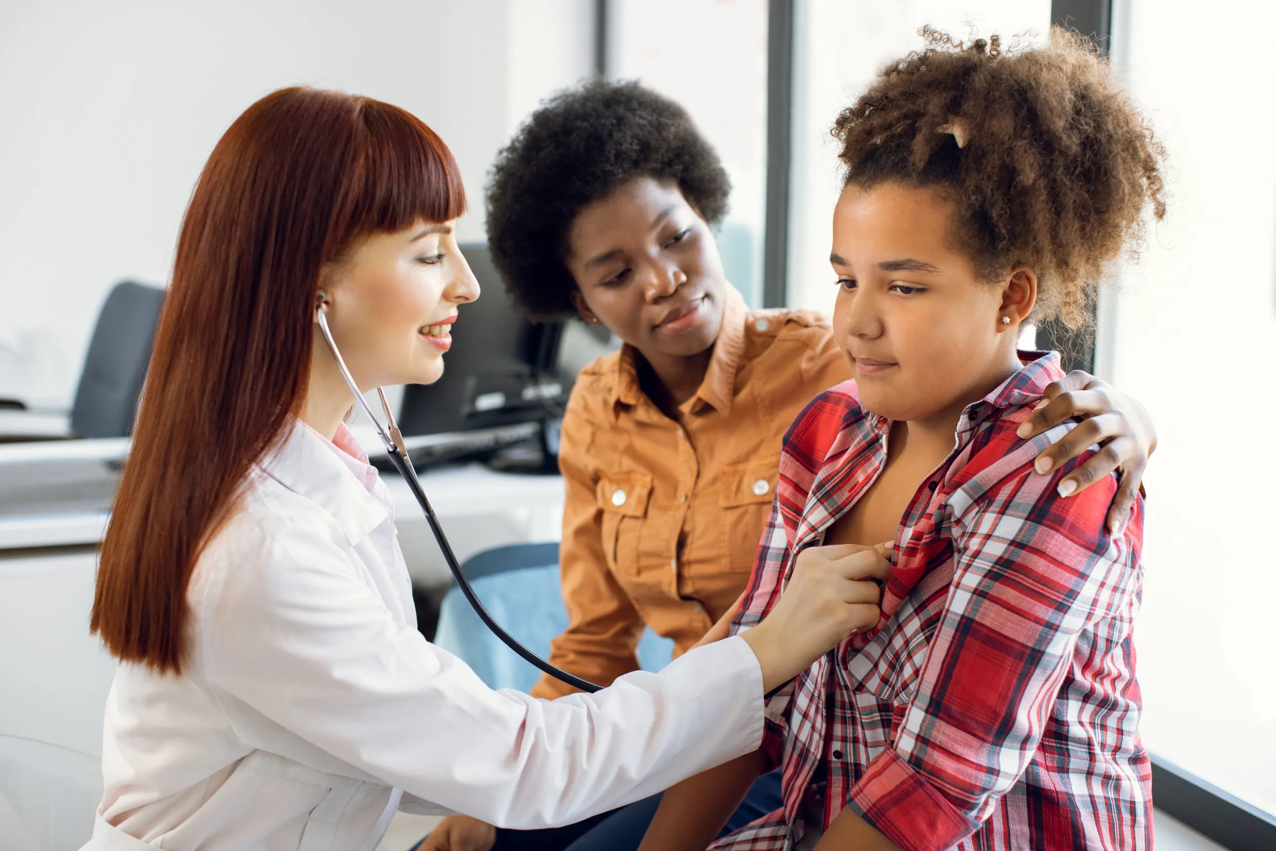 A doctor listening to a girl’s heartbeat with a stethoscope while a woman looks on