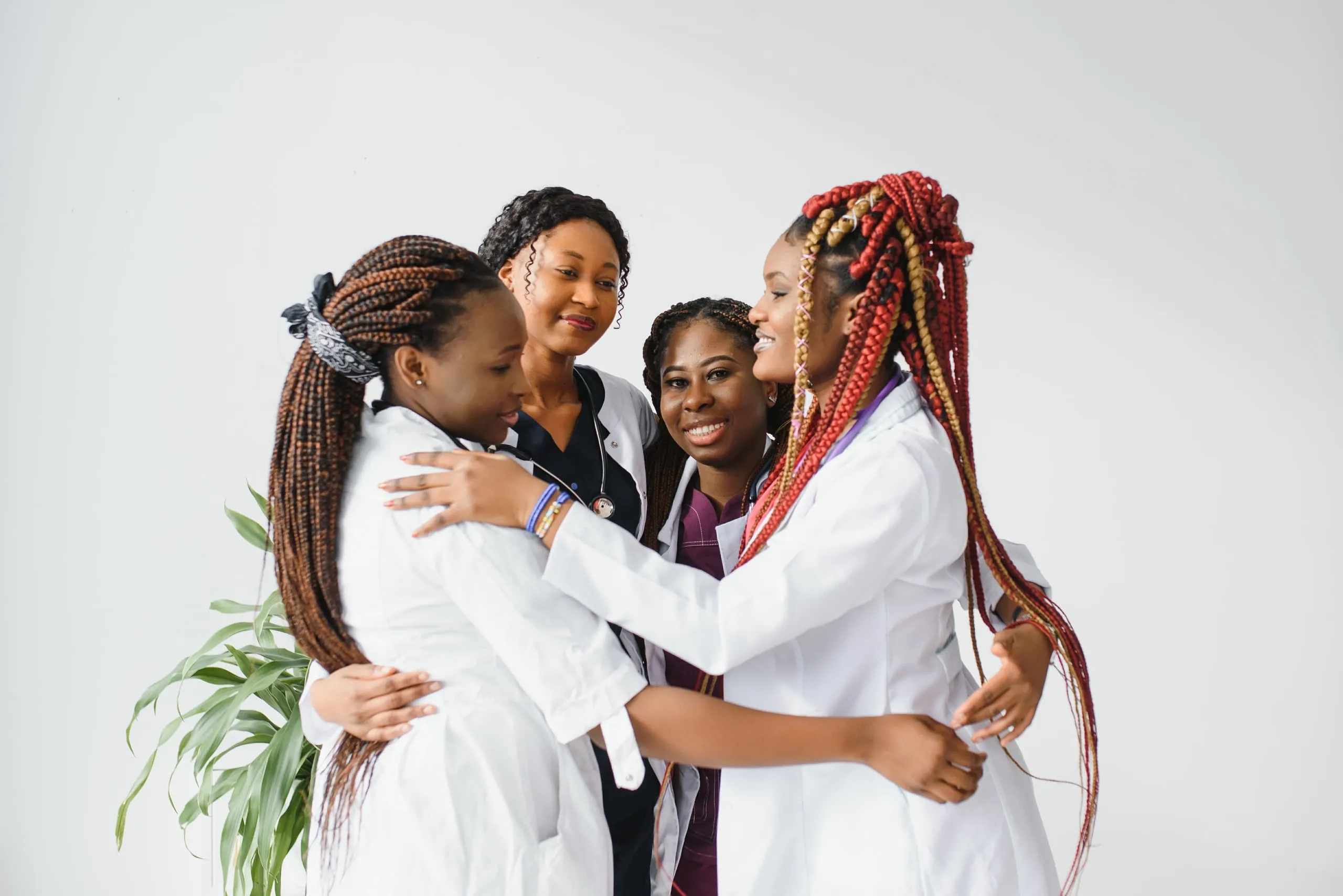 Four health workers in white coats hugging and smiling