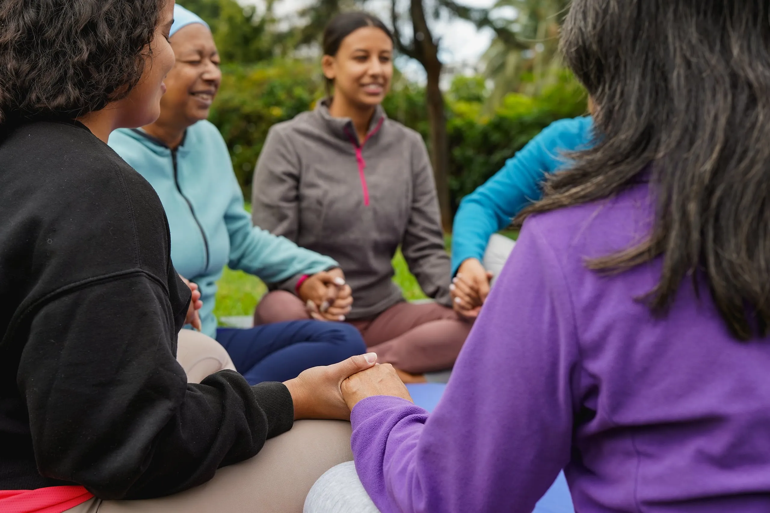 Women sitting in a circle outdoors, holding hands