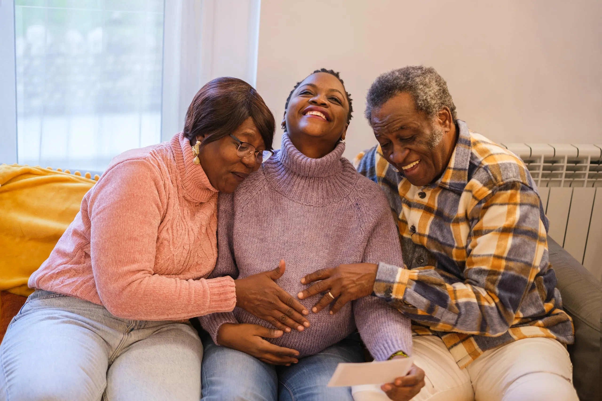A smiling woman sitting on a sofa between a younger woman and a man