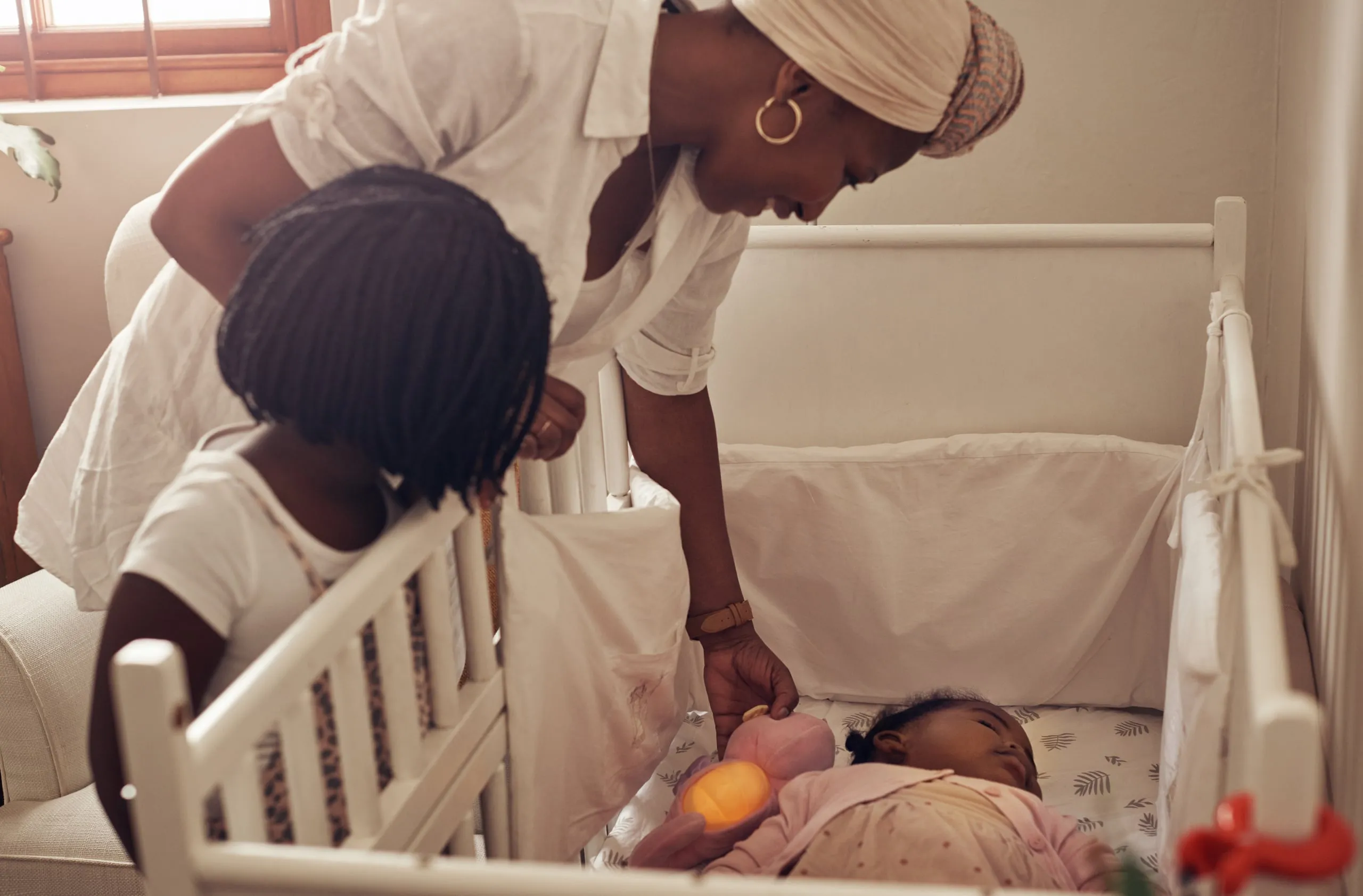 A mother and her young child looking at a baby in a cot