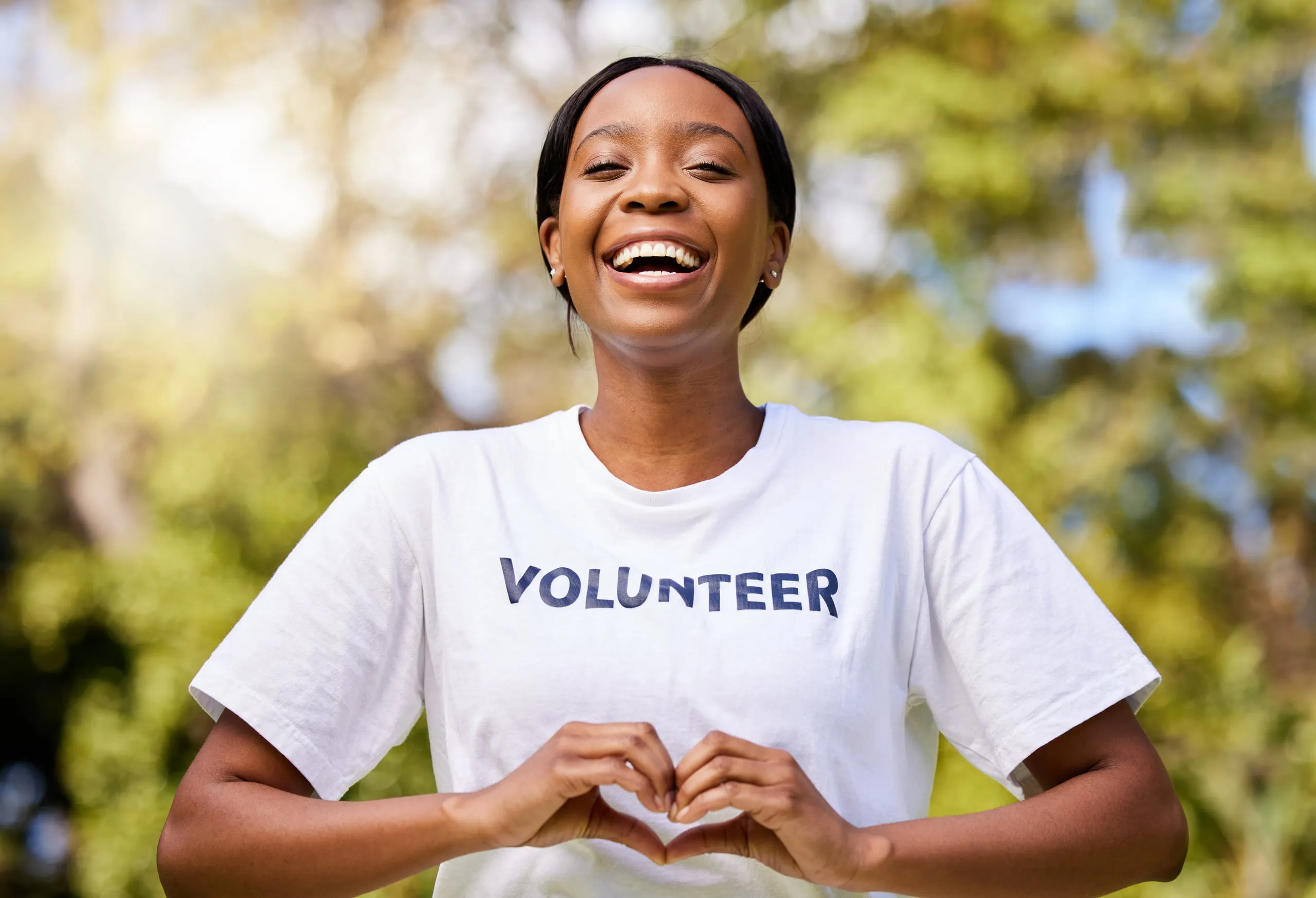 A smiling volunteer in a “Volunteer” T-shirt making a heart with her hands