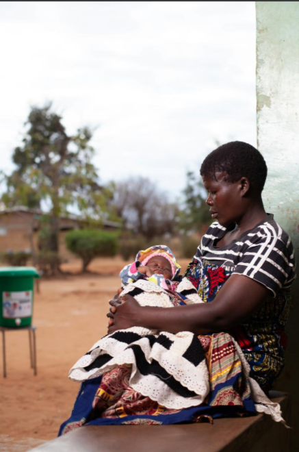 A mother cradling her newborn outside her home